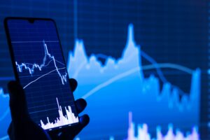 Close-up of a investor's hand holding a phone displaying volatile stock market charts.