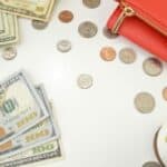 Dollar bills, coins, and red wallet arranged on white surface with succulent plant